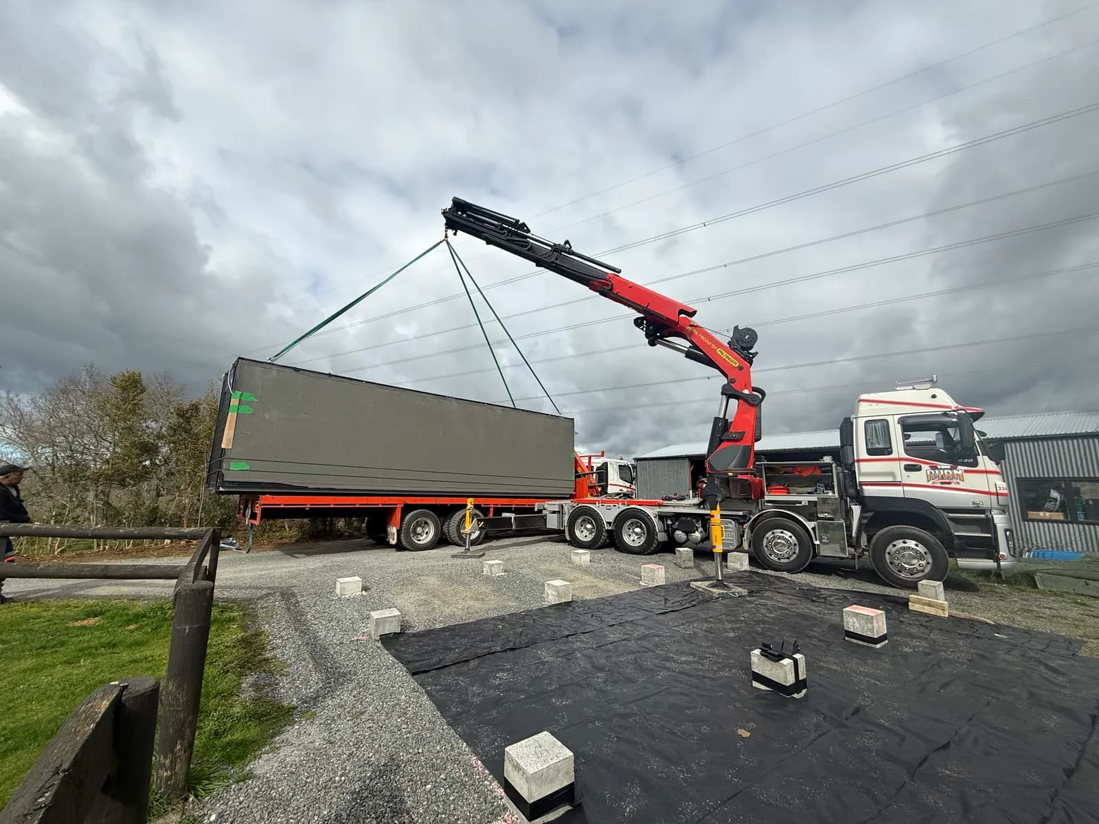 Crane truck swinging a folded module onto a prepared gravel pad