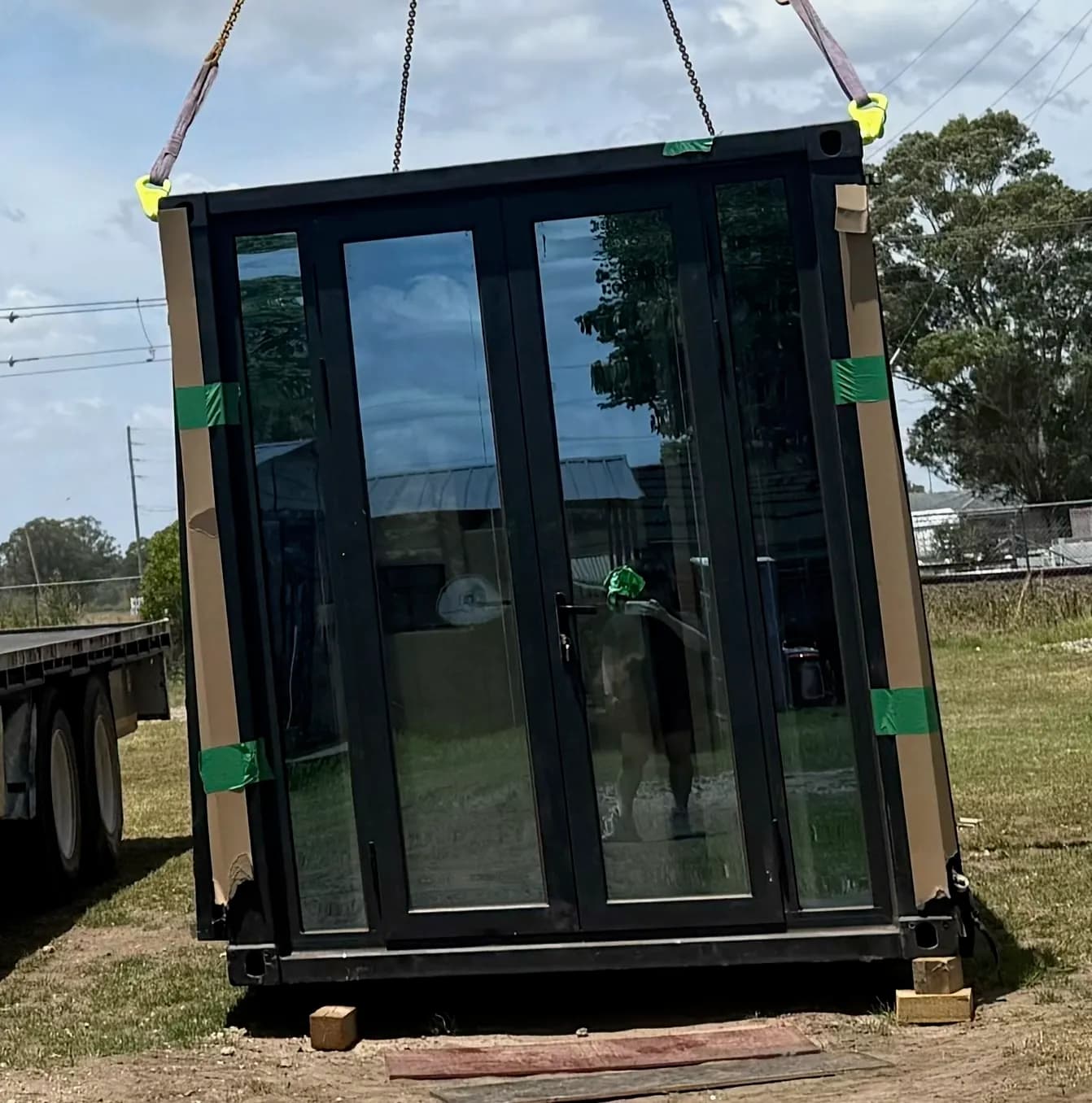 Folded home with full-height glazing strapped to a trailer, edges taped for transport