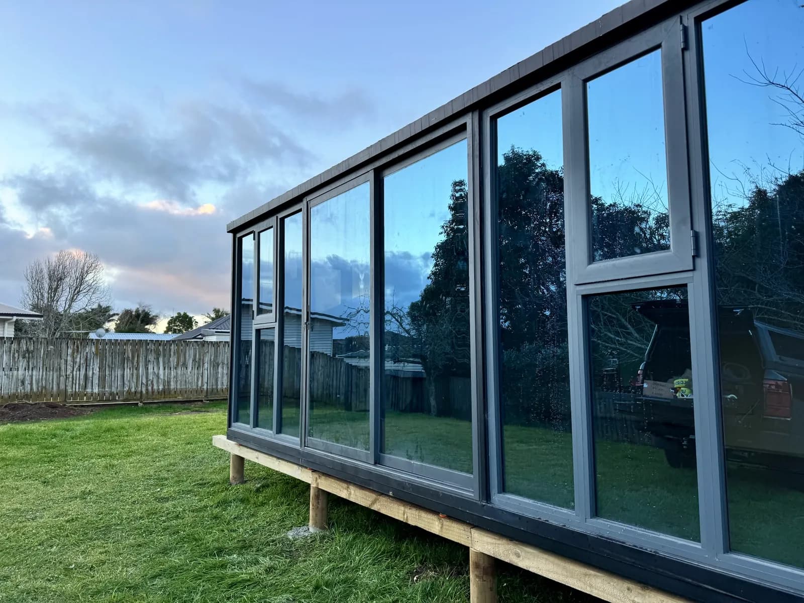 Studio with floor-to-ceiling glazing on timber bearers in a backyard at dusk