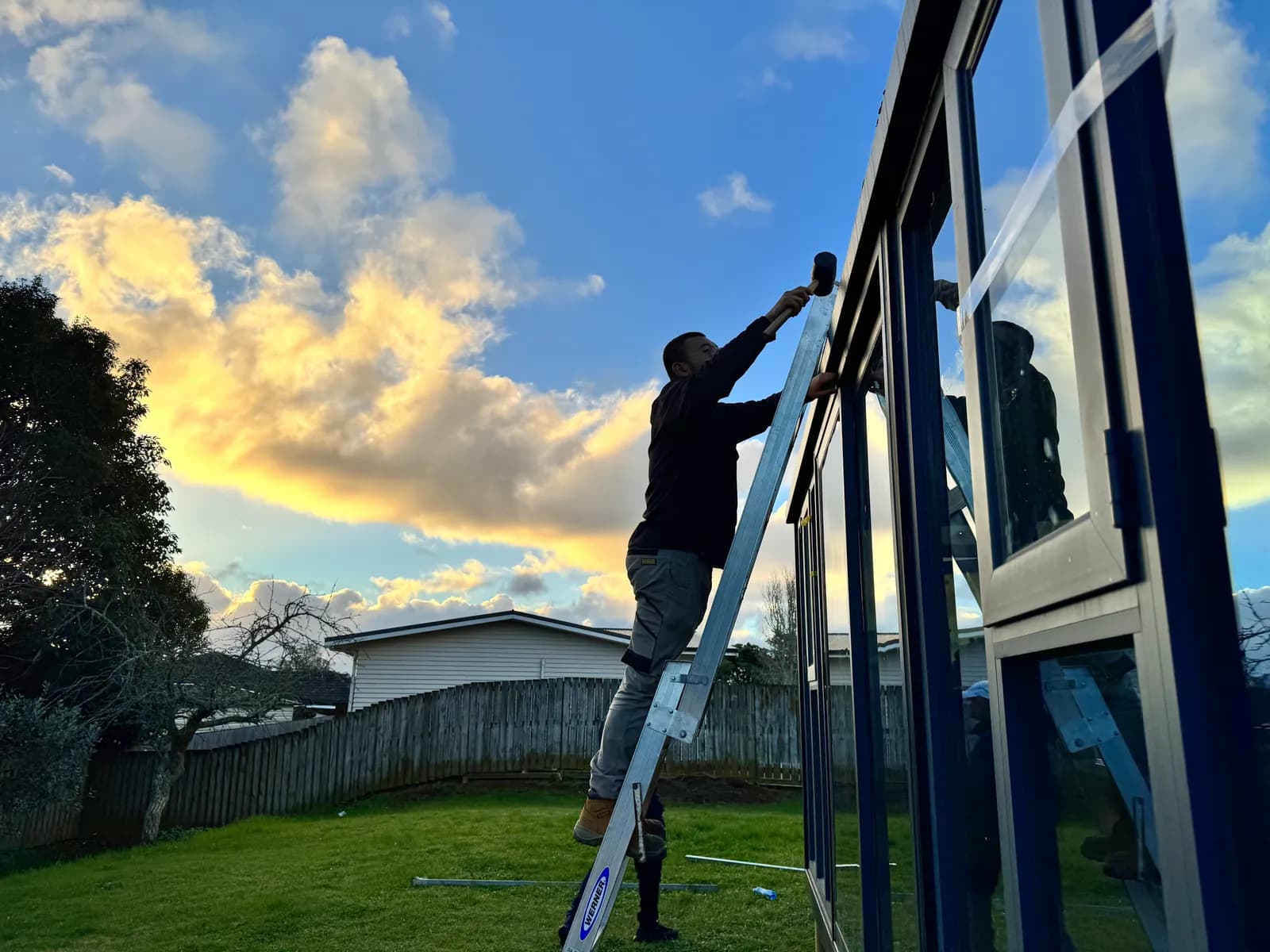 Installer on a ladder fitting glazing to a Studio at sunset