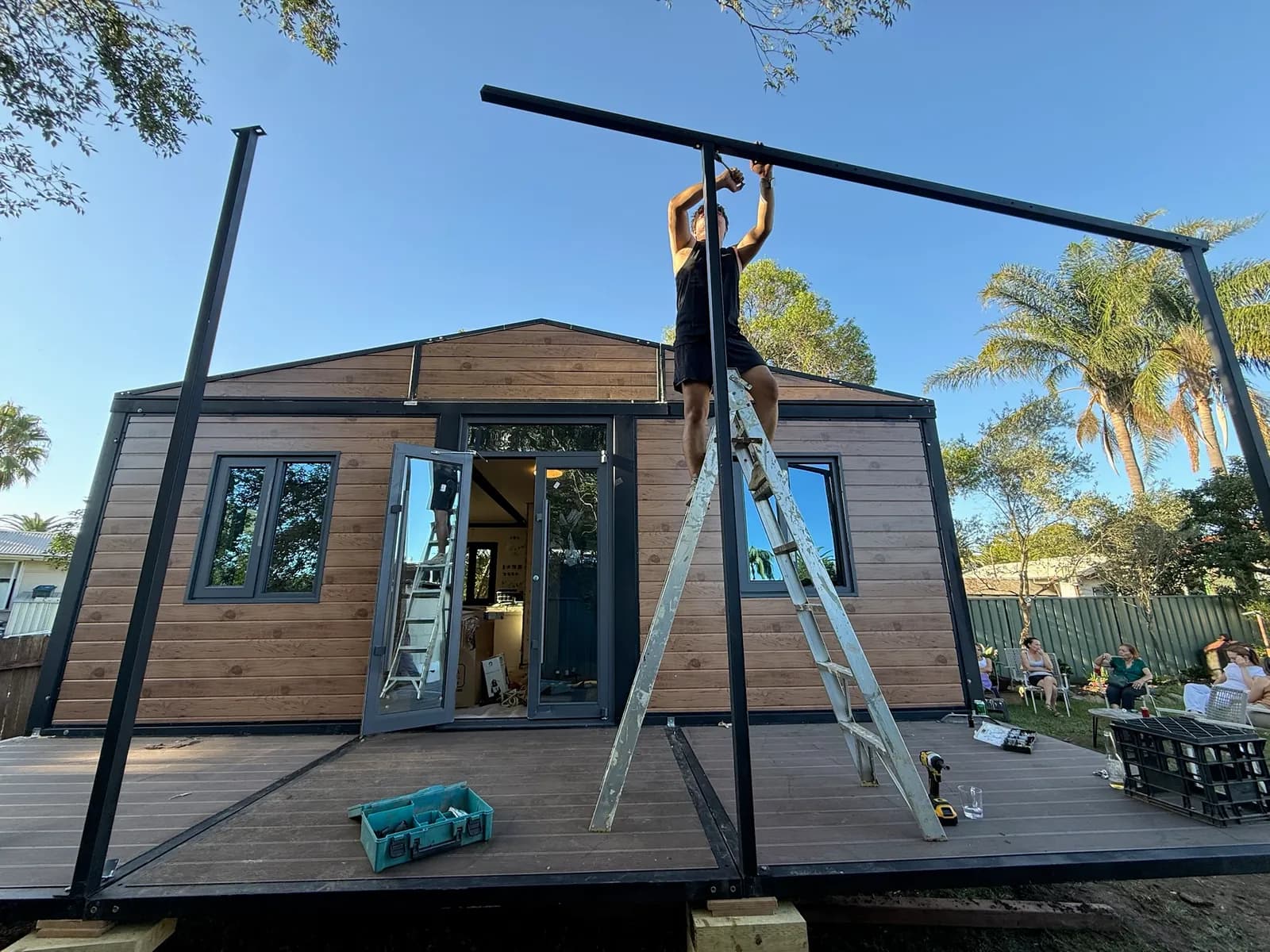 Rex on a ladder lifting a roof beam into place over the deck