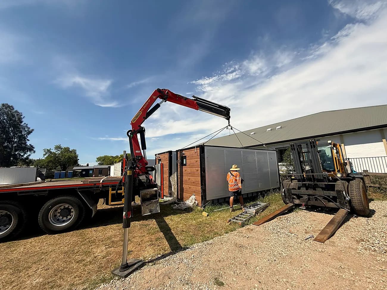 Truck-mounted crane lifting a folded unit off a trailer at a residential site