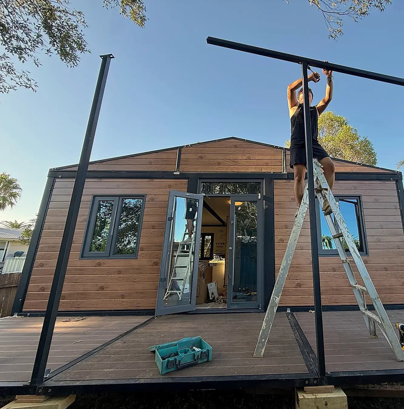 An installer on a ladder fitting the roof frame of a timber-clad unit