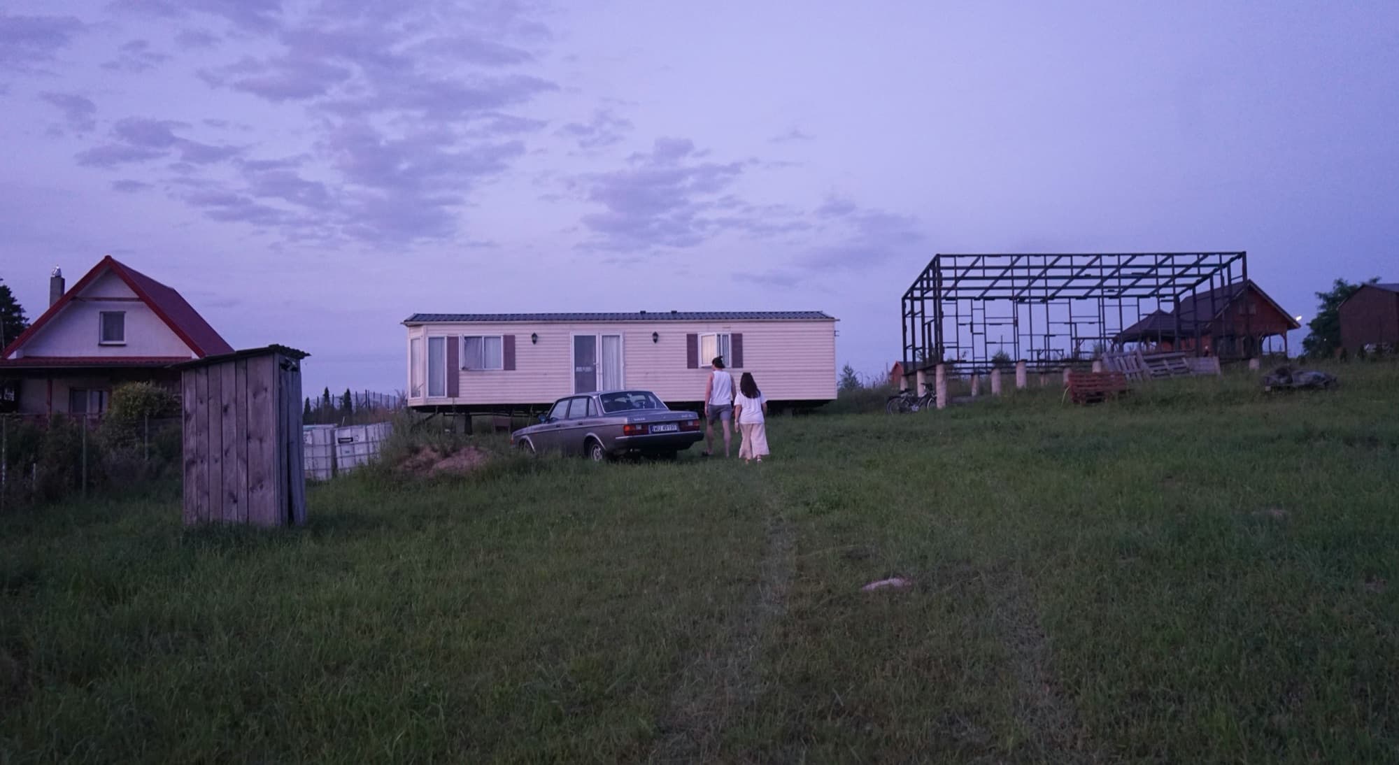 A transportable dwelling placed on a rural section beside a new building frame at dusk