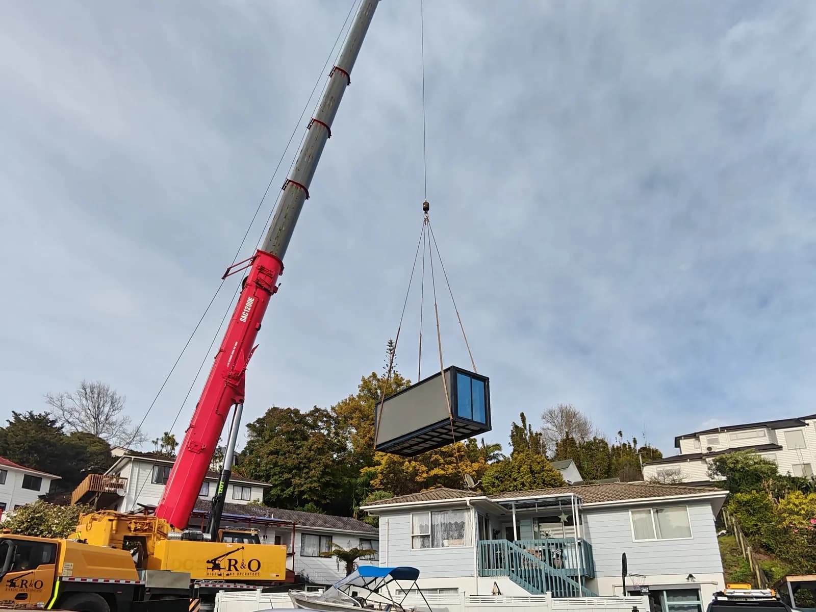 Crane lifting a Comfort 20 module over a house towards the backyard