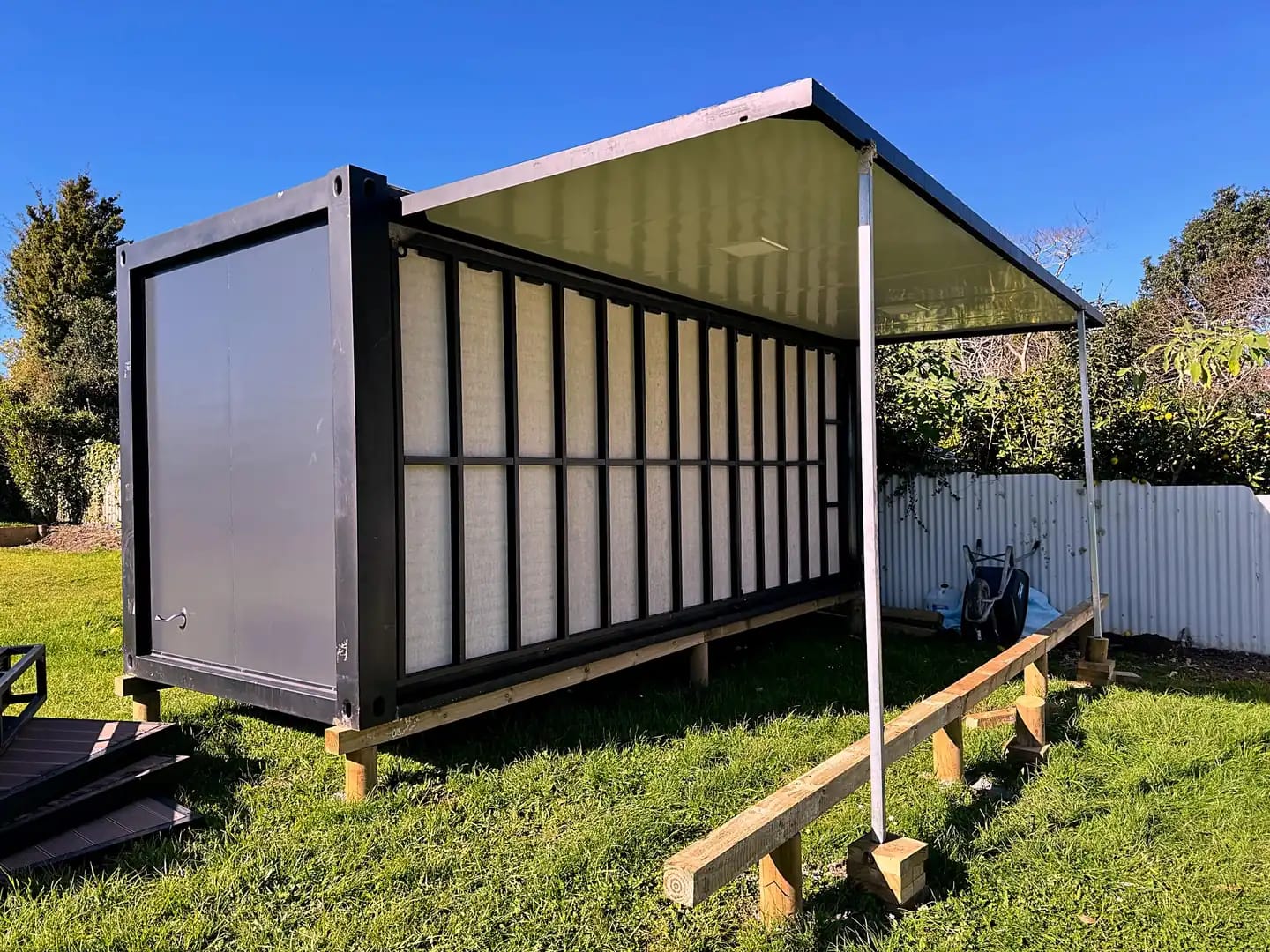 Expandable unit mid-unfold in a backyard, roof wing raised on props
